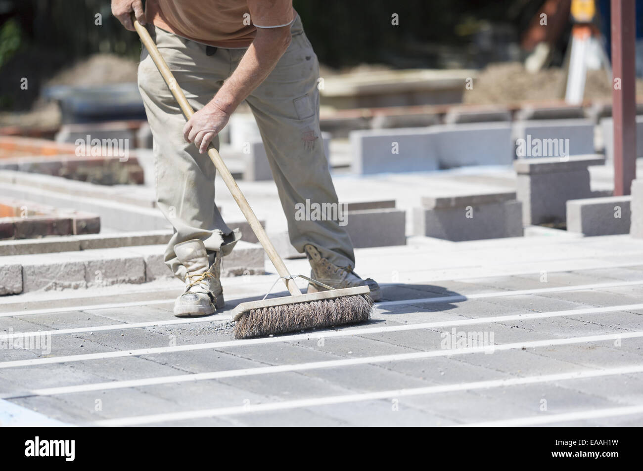 A man using a brush on a cement floor on a construction site. Stock Photo