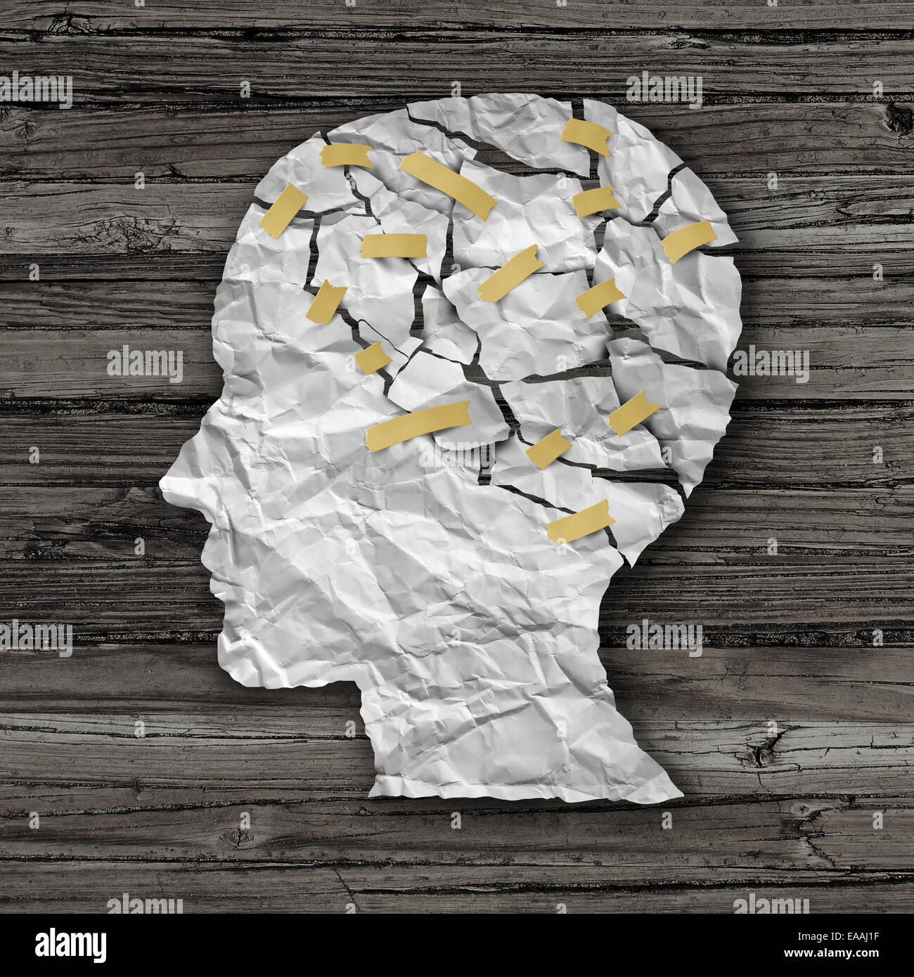 Brain disease therapy and mental health treatment concept as a sheet of torn crumpled white paper taped together shaped as a side profile of a human face on wood as a symbol for neurology surgery and medicine or psychological help. Stock Photo