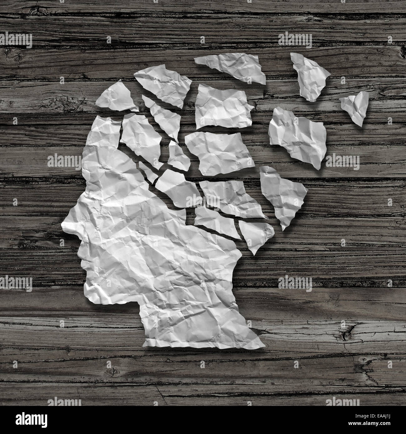 Alzheimer patient medical mental health care concept as a sheet of torn crumpled white paper shaped as a side profile of a human face on an old grungy wood background as a symbol for neurology and dementia issues or memory loss. Stock Photo