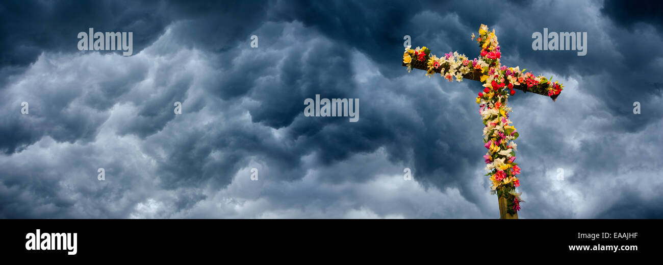 Cross Decorated with Flowers: A cross in front of storm clouds has been decorated with flowers signifying that Christ is alive. Stock Photo