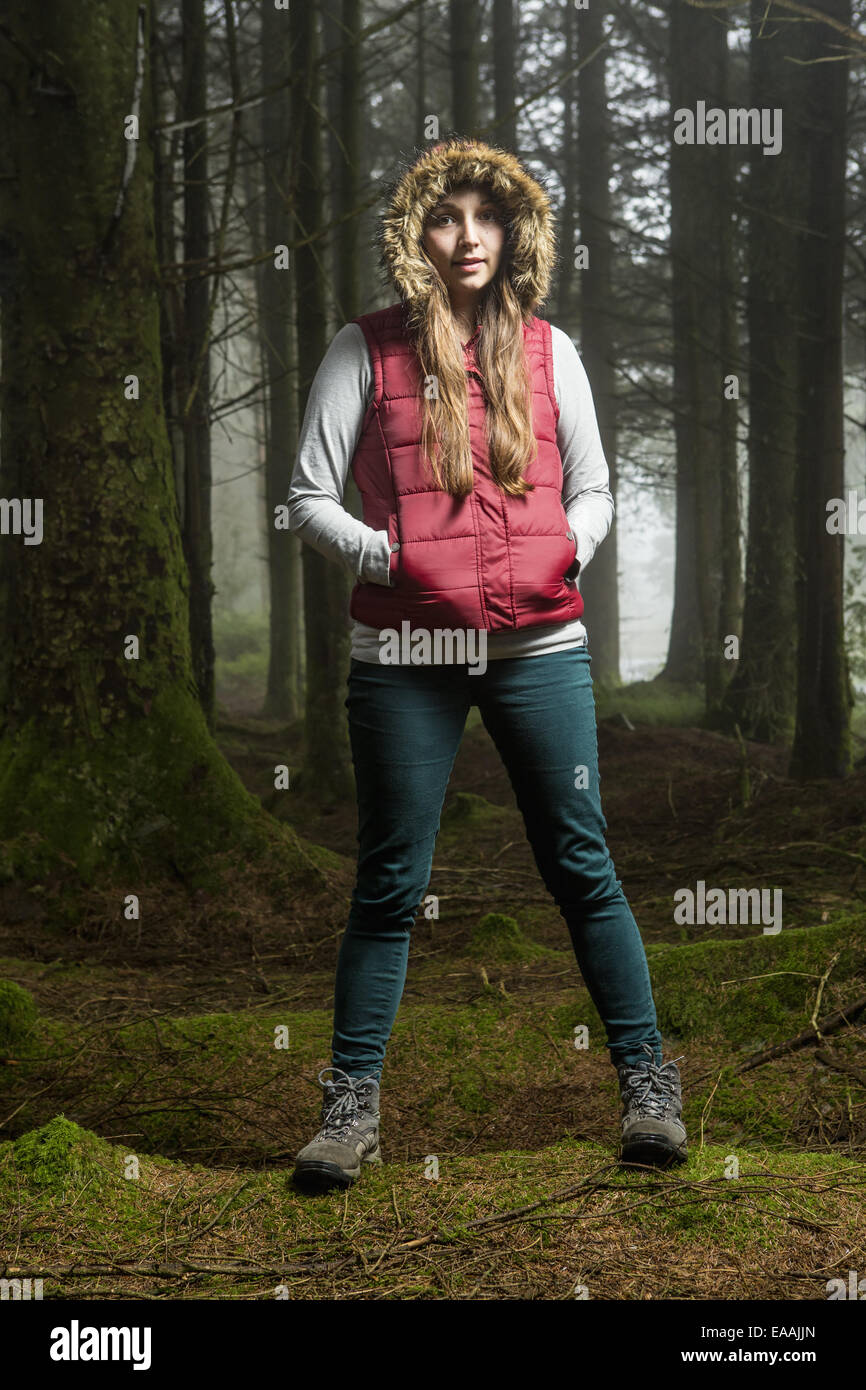 A young woman standing in a forest with her hood up and hands in her pockets. Stock Photo