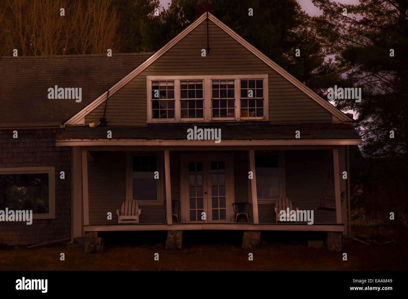 Old, rustic Maine house with porch in late evening light. White trim in