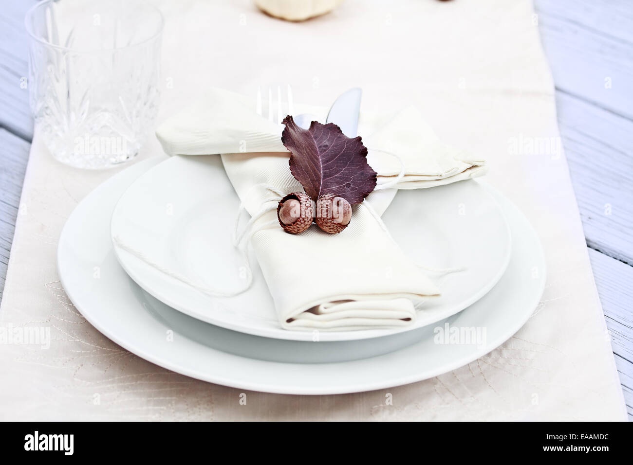 Rustic table decorated with leaves and acorns, ready for a Thanksgiving meal. Stock Photo