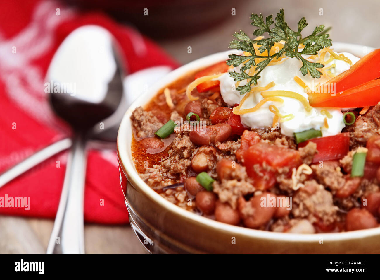 Bowl of Chili Con Carne garnished with sour cream, chives and cheddar cheese. Shallow depth of field with selective focus. Stock Photo