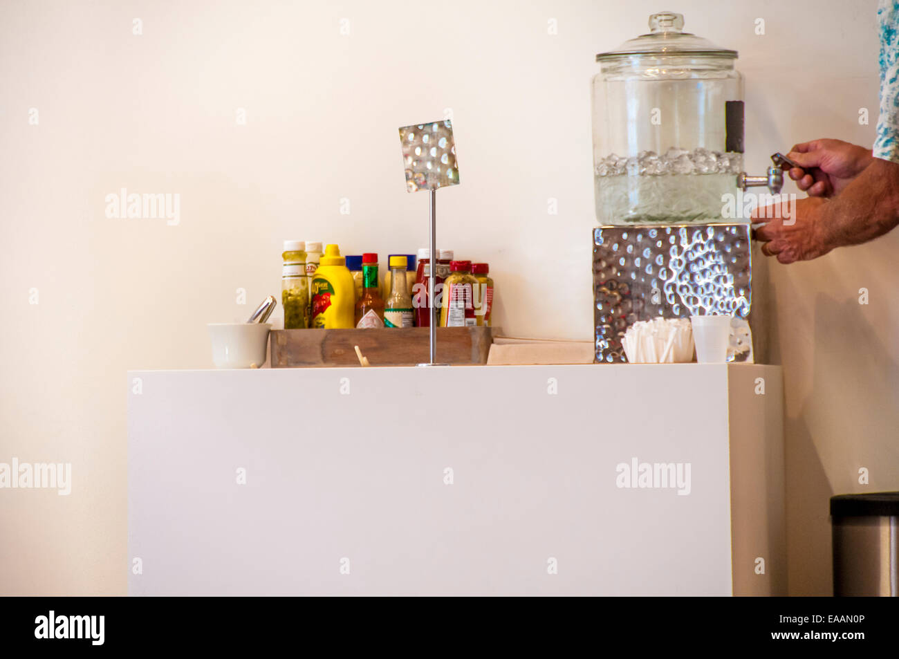 Man filling cup at a Condiment and water fountain setup in a museum. Stock Photo