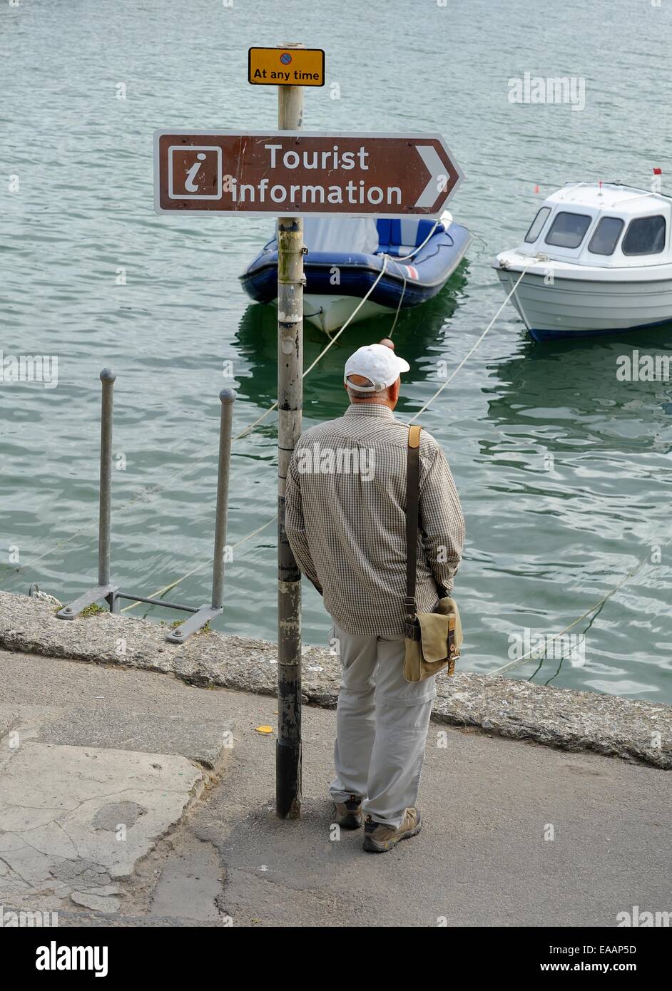 An elderly senior man leaning against a signpost with a brown tourist information sign.Padstow Cornwall,England uk Stock Photo