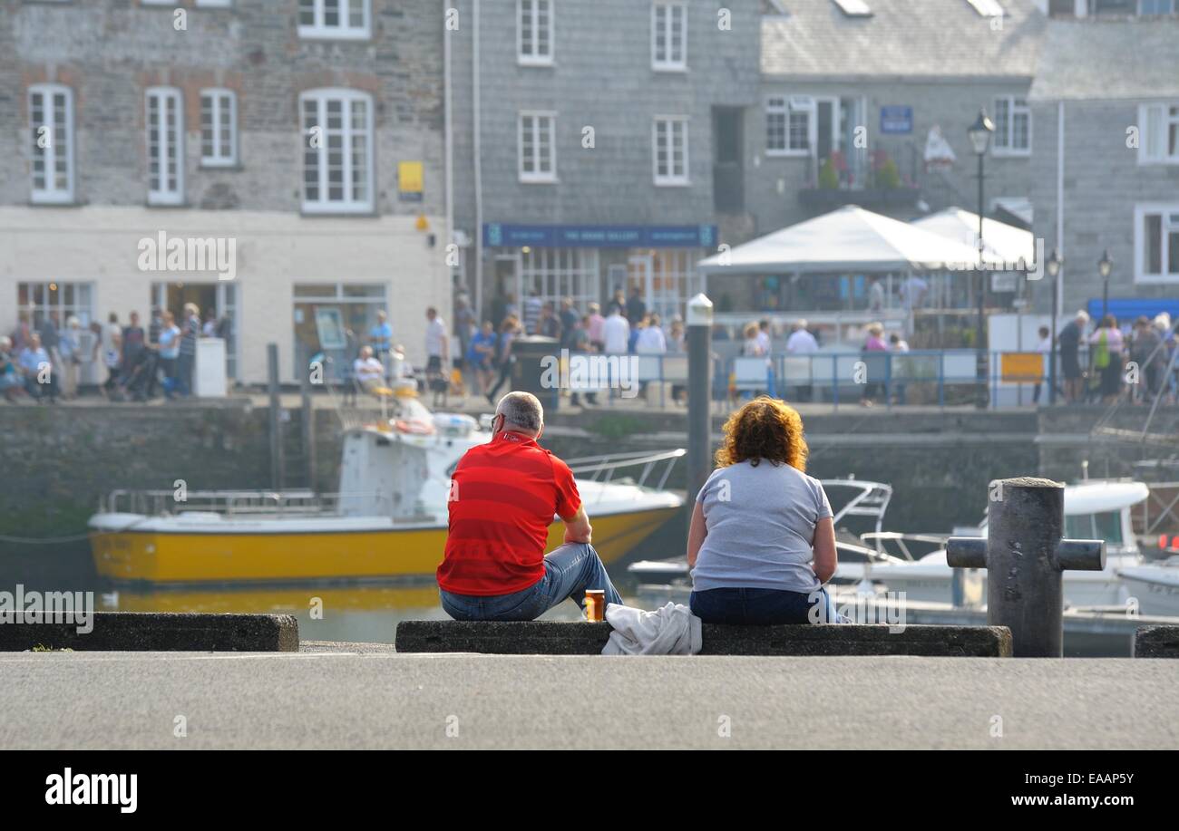 A middle aged couple sitting on the harbour quayside drinking beer. Padstow Cornwall England uk Stock Photo