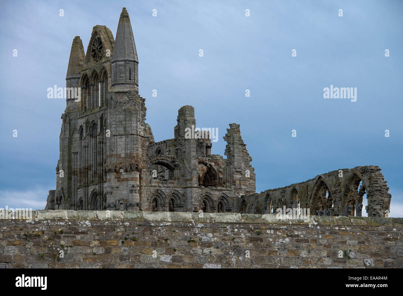 Whitby Abbey in North Yorkshire, England, with stone wall in foreground dark clouds behind Stock Photo
