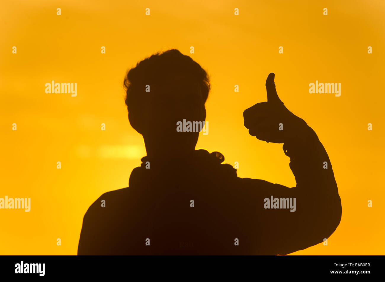 Silhouette of a man at sunrise giving a thumbs up sign. Stock Photo