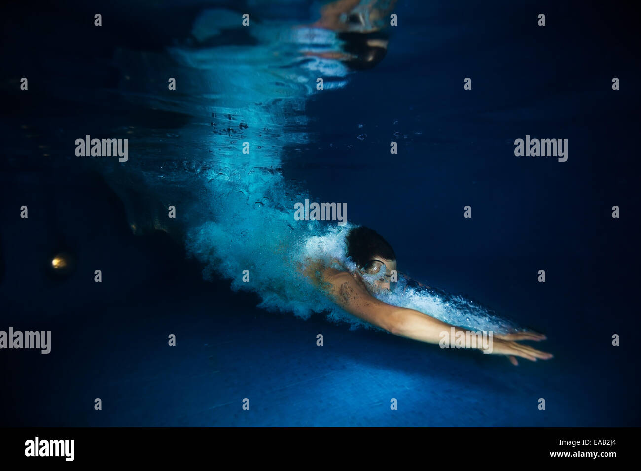 Man with splash swimming under dark blue water Stock Photo