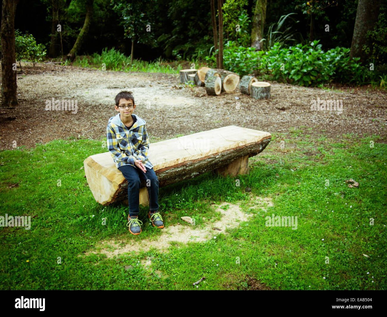 Boy sits on sawn log bench in park Stock Photo