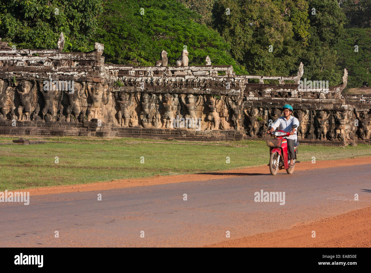 Cambodia, Angkor Thom.  Man on Motor Bike Going Past the Elephant Terrace. Stock Photo