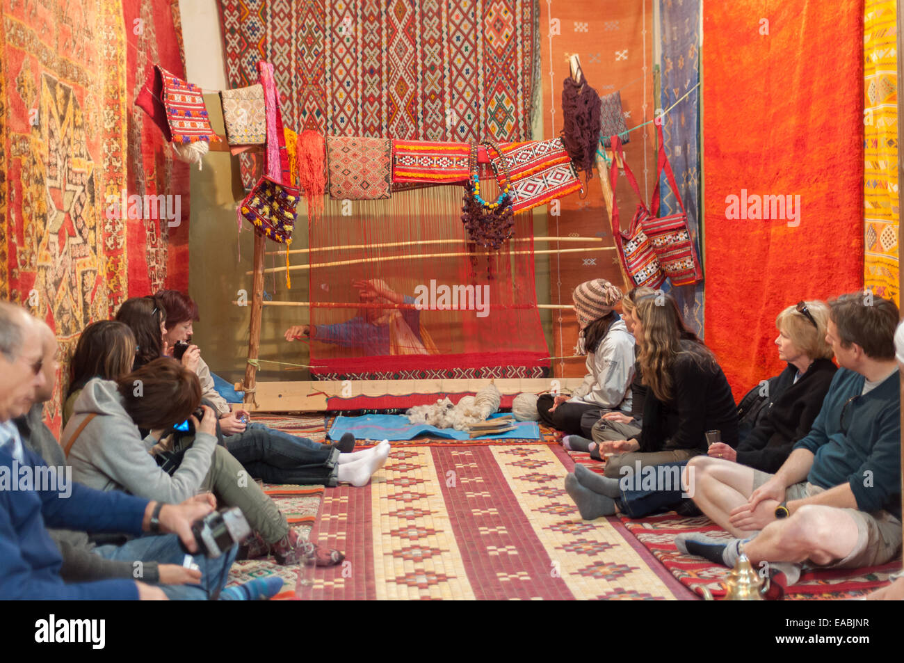Tourists watching moroccan woman weaving traditional carpet. Morocco, Africa Stock Photo
