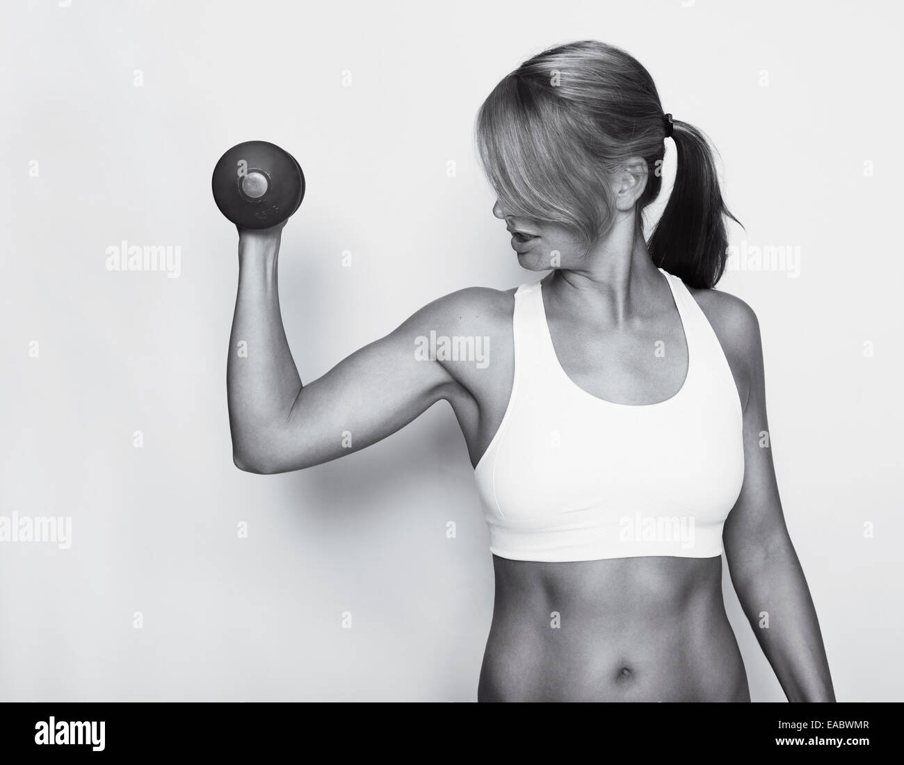 a woman in a white sports top trained their upper arms with dumbbells, black and white Stock Photo