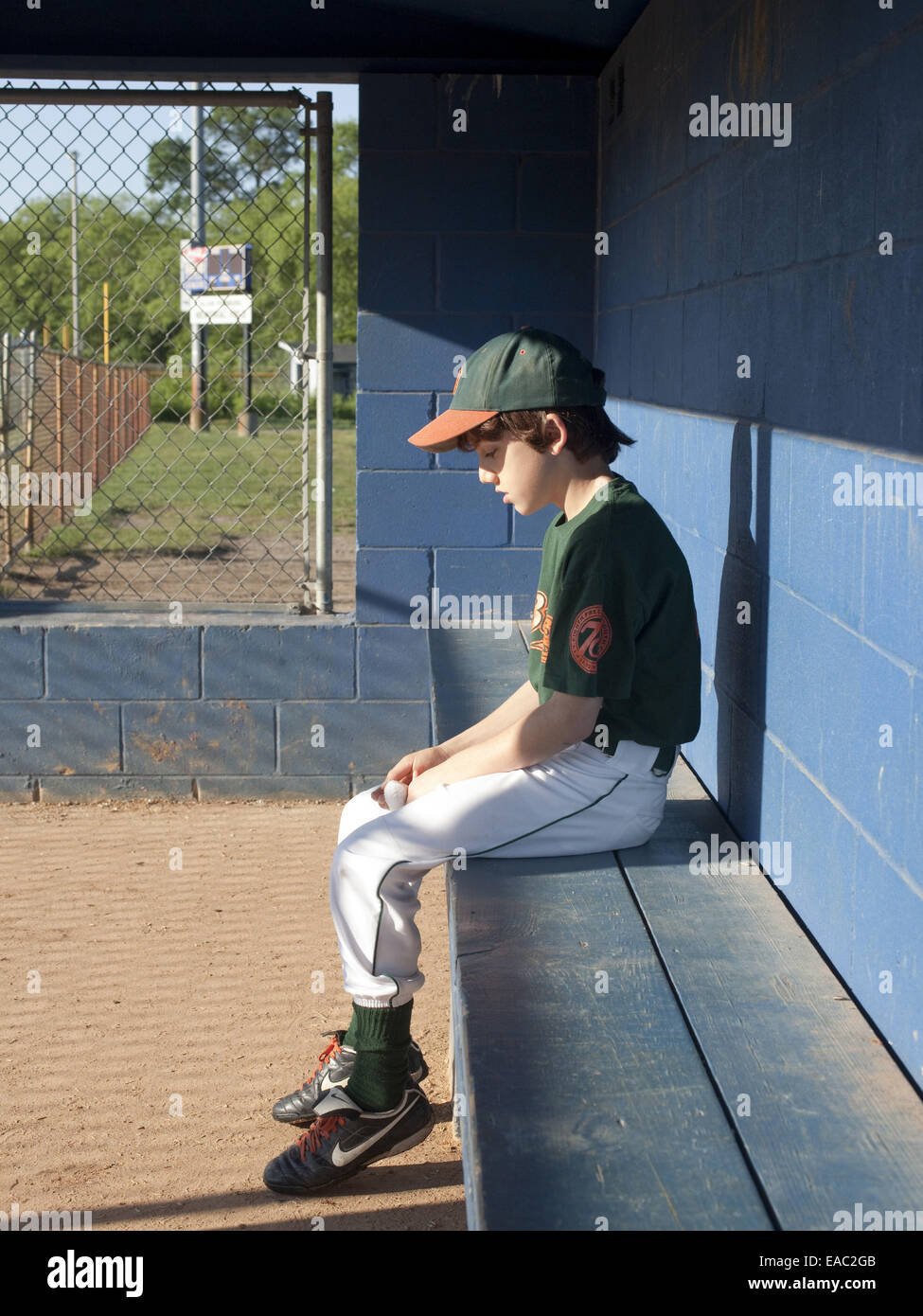 sad boy sitting alone in baseball dugout Stock Photo
