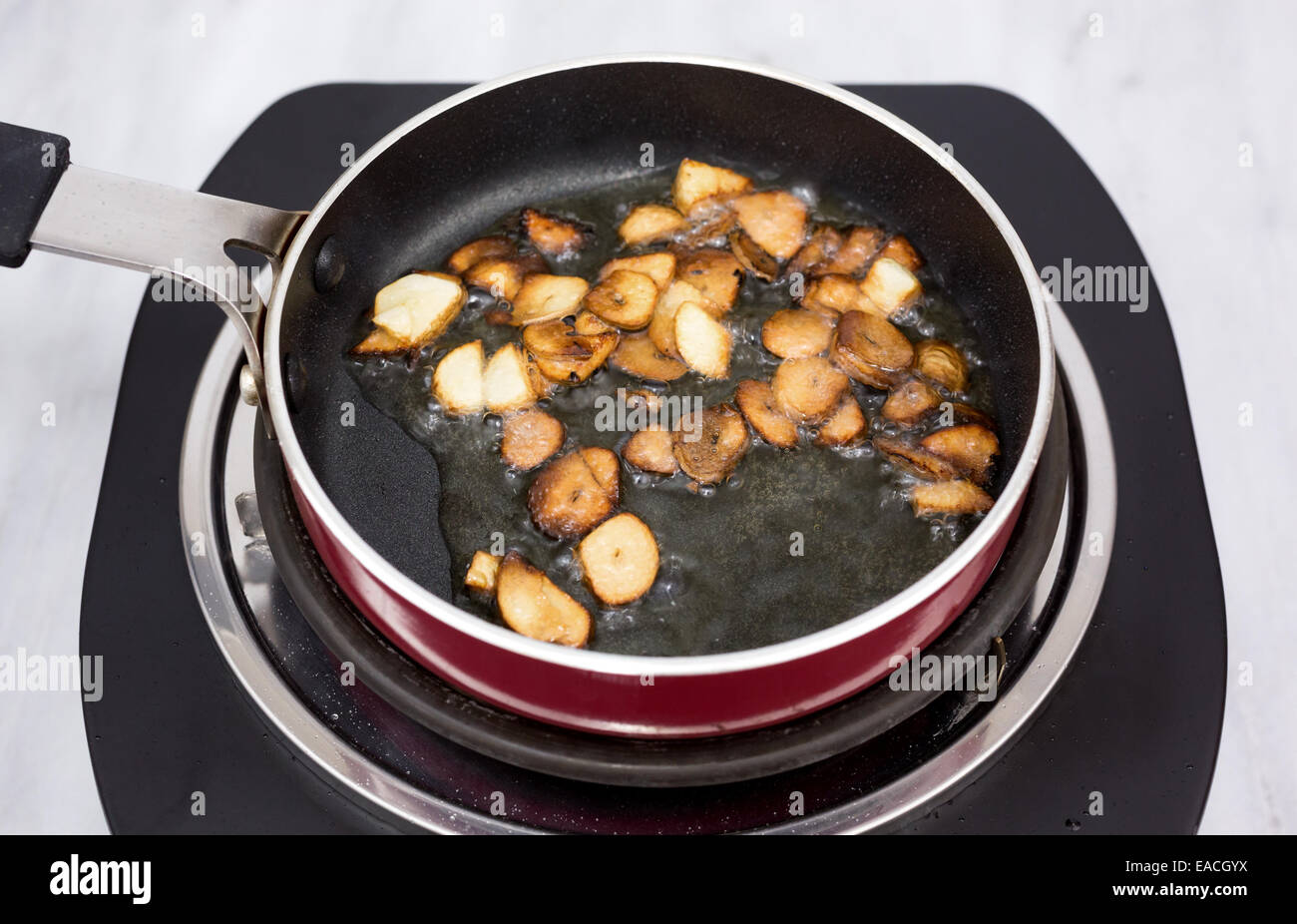 A small frying pan cooking sliced garlic in olive oil on a small single