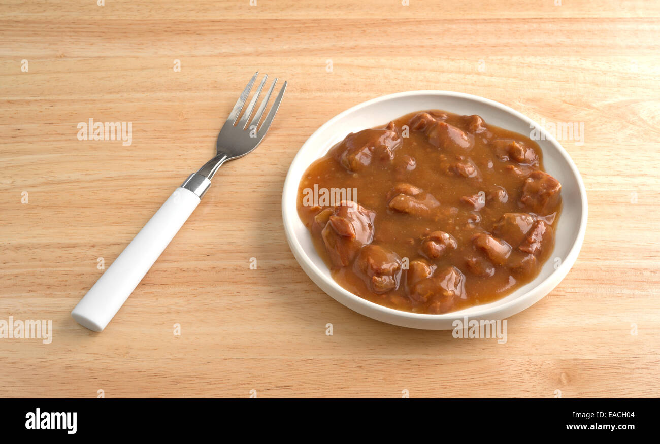 A small serving of roast beef in gravy with a fork to the side atop a wood table. Stock Photo