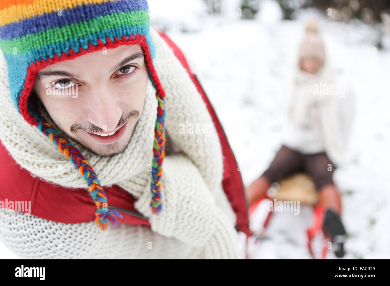 Man carrying woman in sled though snow in winter Stock Photo