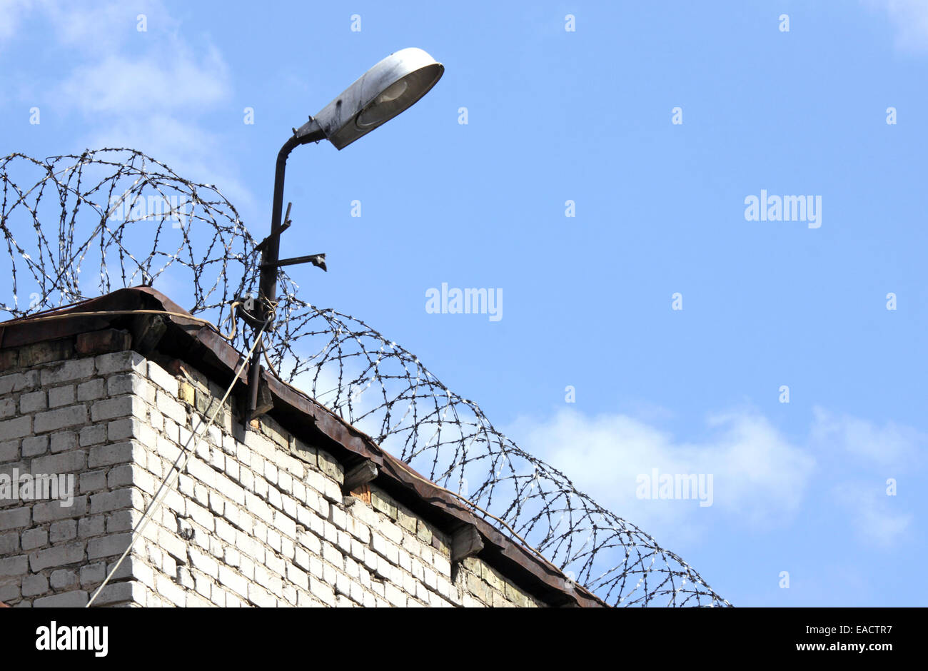 Detail of the brick prison wall with fence and lamp Stock Photo