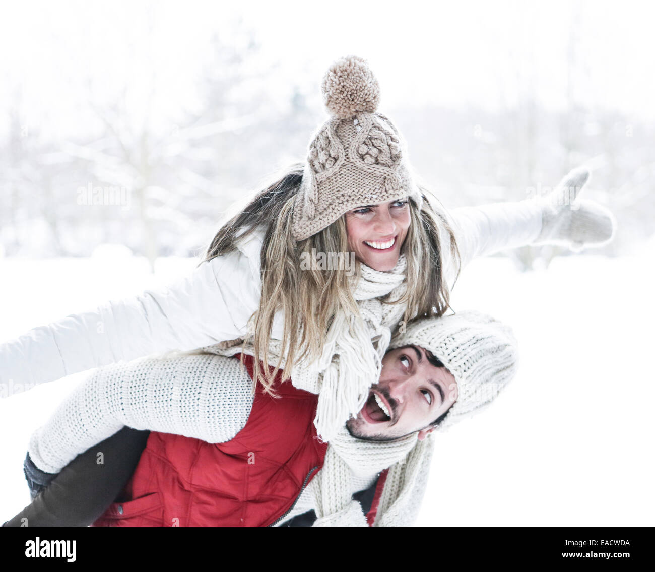 Happy man carrying smiling woman for piggyback ride in winter Stock Photo