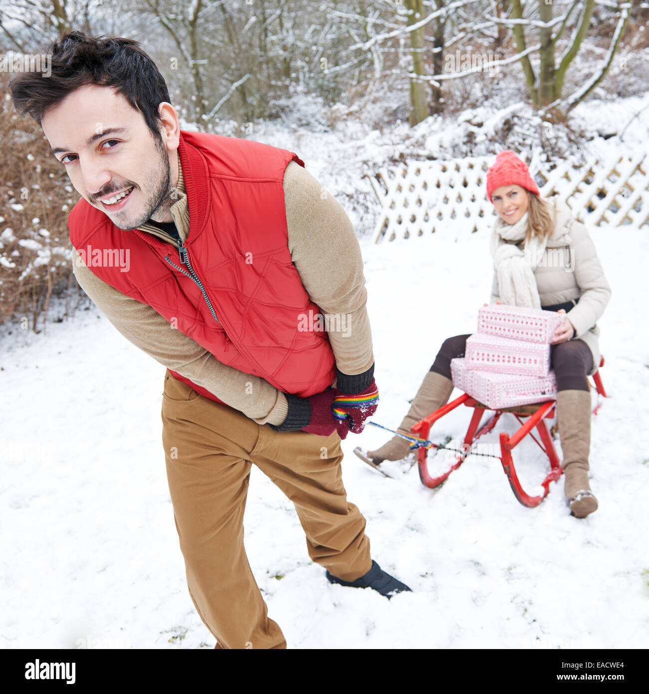 Happy couple sledding in winter with sled with christmas gifts Stock Photo