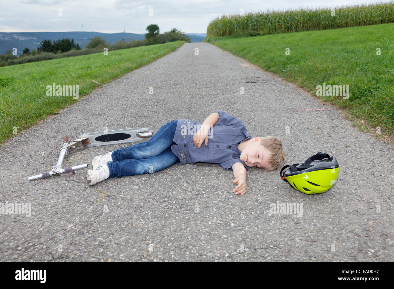 Boy, 5 years, lying on a road after a scooter accident Stock Photo