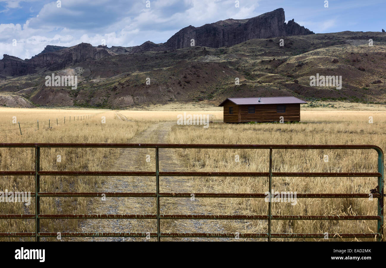 Isolated Log Cabin Flanked By High Rocky Mountains And Grassland