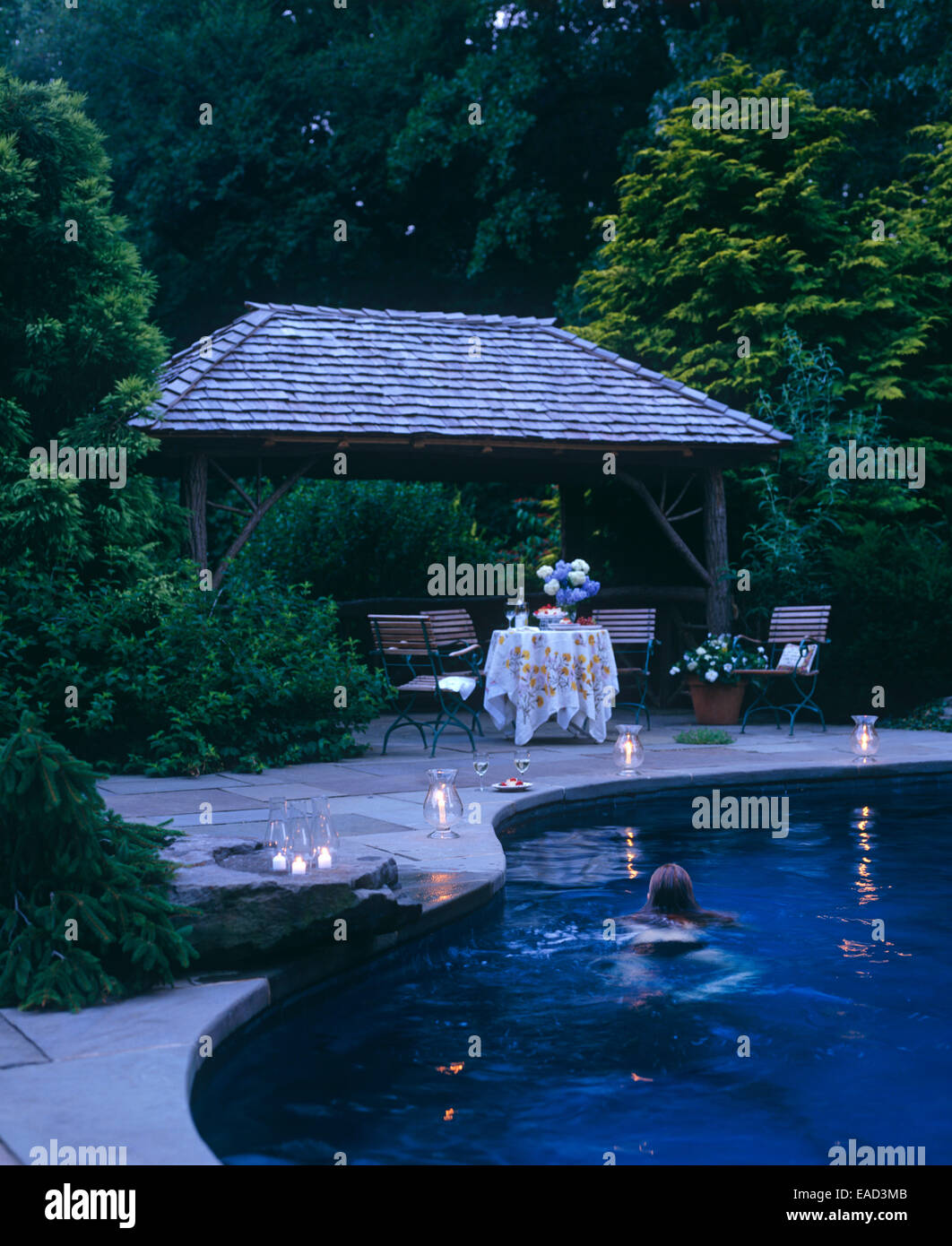 pool at dusk with swimmer and candles Stock Photo