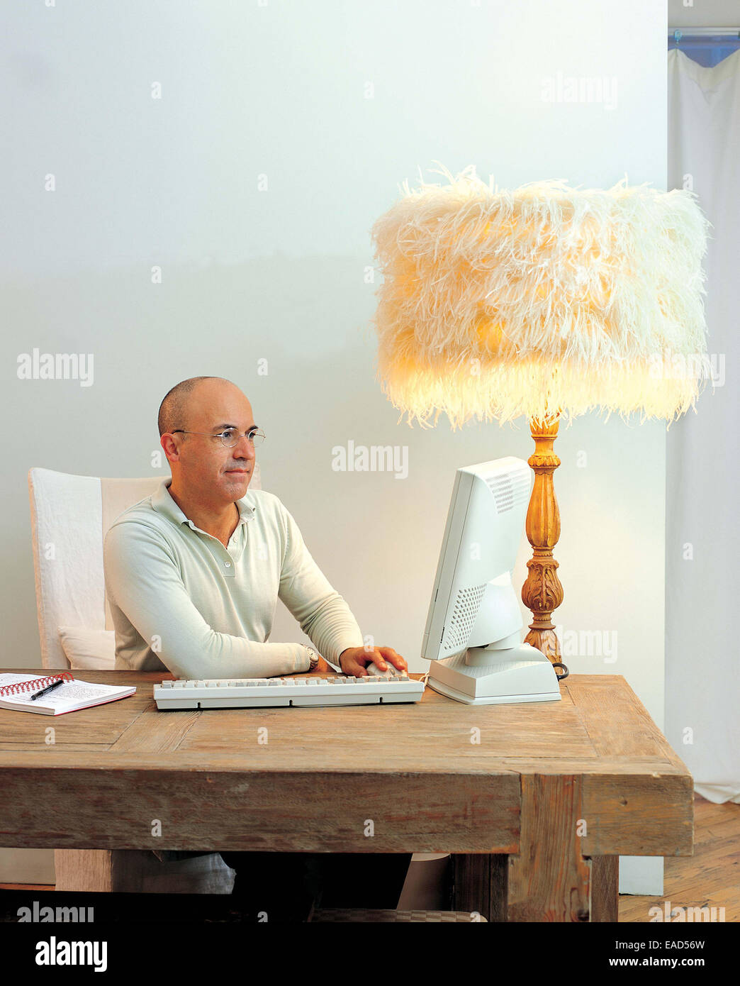 man works at computer with feathered lamp Stock Photo