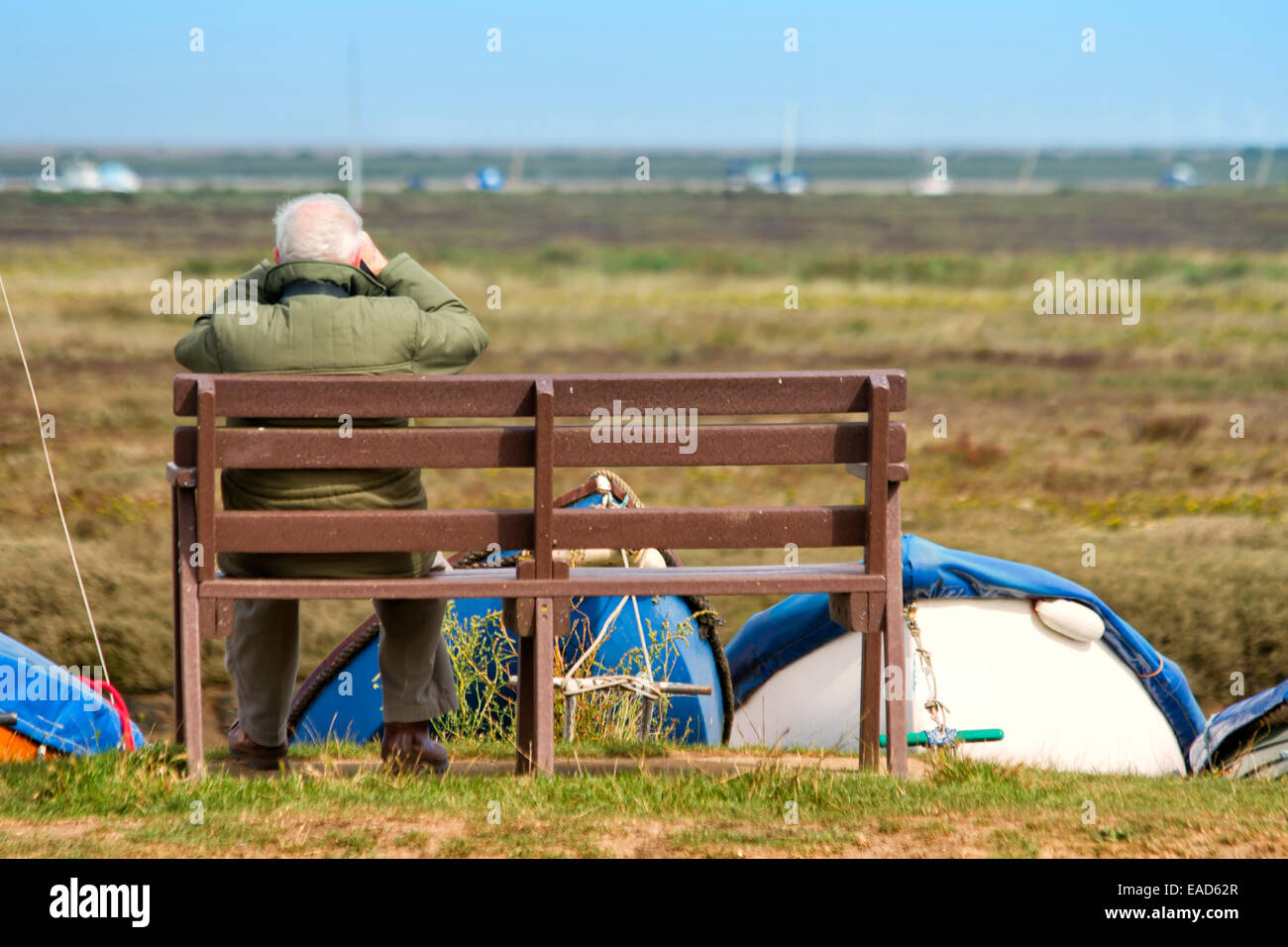 Elderly man sitting on a bench, viewing the salt marsh through