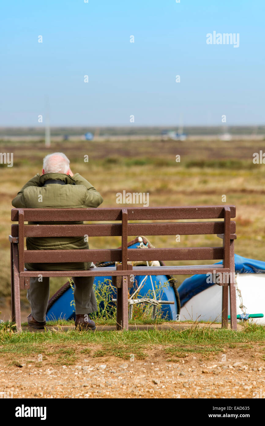 Elderly man sitting on a bench, viewing the salt marsh through