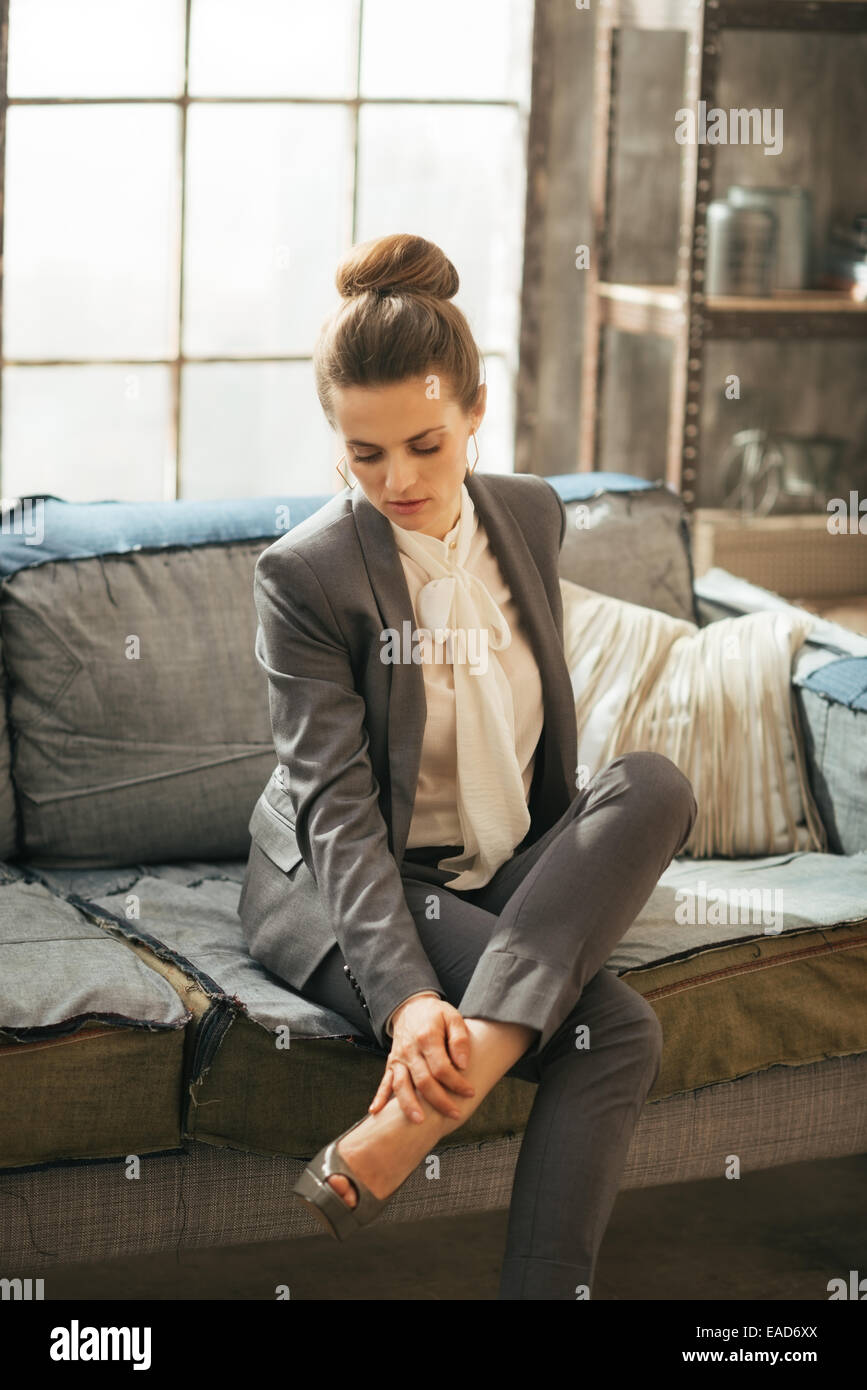 Thoughtful business woman in loft apartment checking tired legs Stock Photo