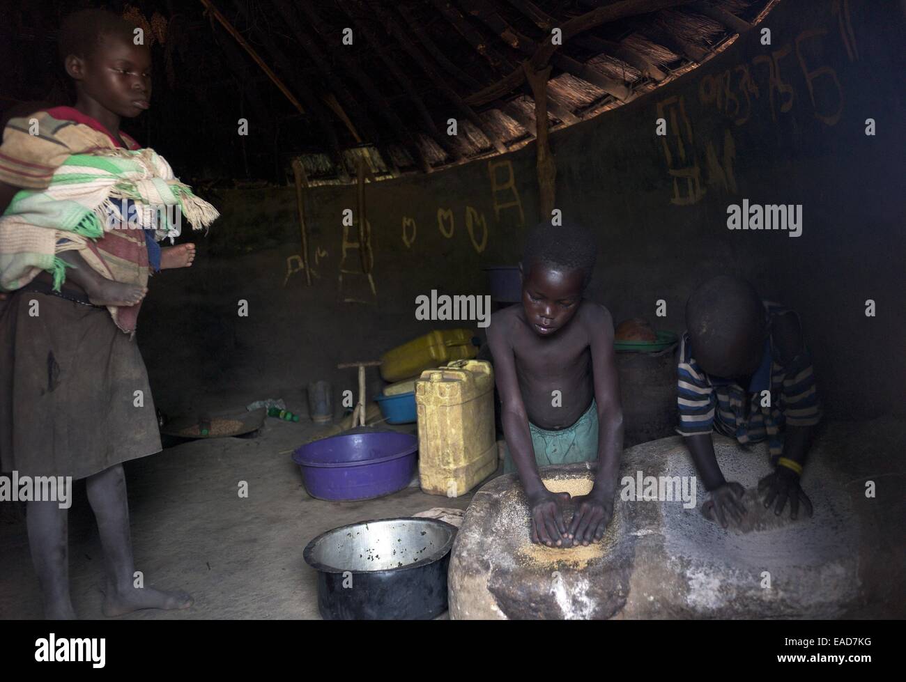 Cogong Village, Agago District, Uganda. 17th July, 2014. July 17, 2014 - Codong Village (Agago District) - Alimo Agnes, 10, left, returns home from school with her one-year old brother (Kidaga Regan) because he would not stop crying. Her sister Auma Vicky, 7, center, and a neighborhood boy, Ogen, 6 (who didn't know his last name) stayed home from school to crush groundnuts. The hidden cost of schooling is overwhelming in the post-conflict Acholi sub-region. Children constitute an invaluable source of stopgap labour for households re-establishing livelihood strategies. (Credit Image: © Ric Fra Stock Photo