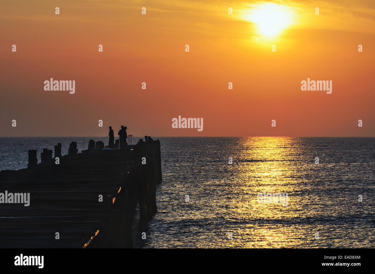 Silhouette fisherman on the old wooden bridge and sea at sunrise in rural Thailand. Stock Photo