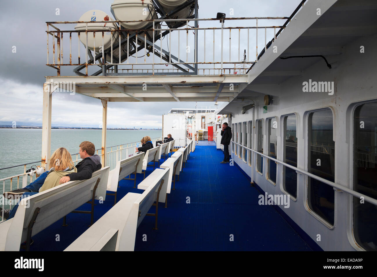 Passengers sitting on seats on a deck of a ferry under a Zodiac Liferaft deployment slide Stock Photo