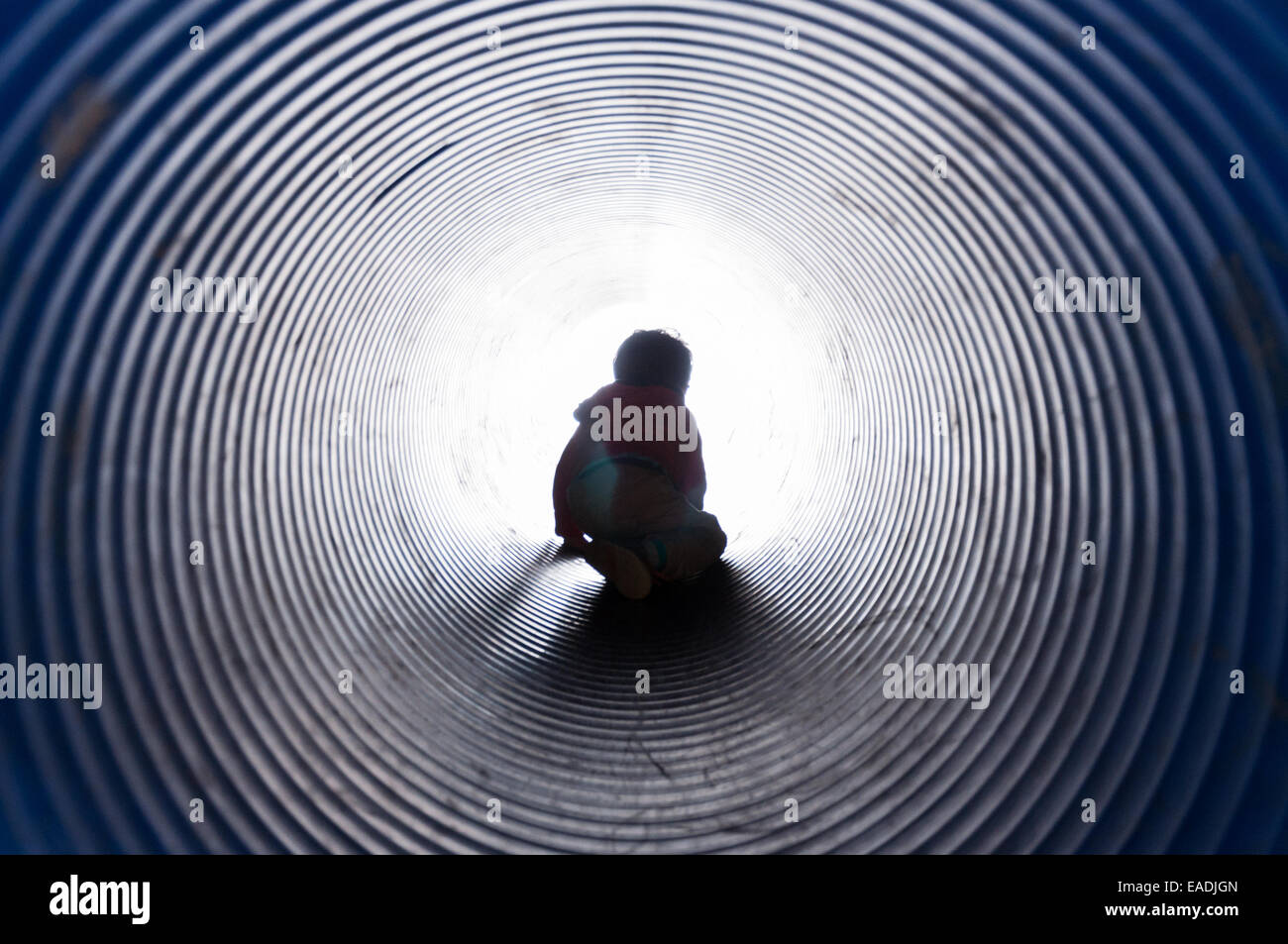 Boy climbing through a tunnel with light at the end of the tunnel Stock Photo