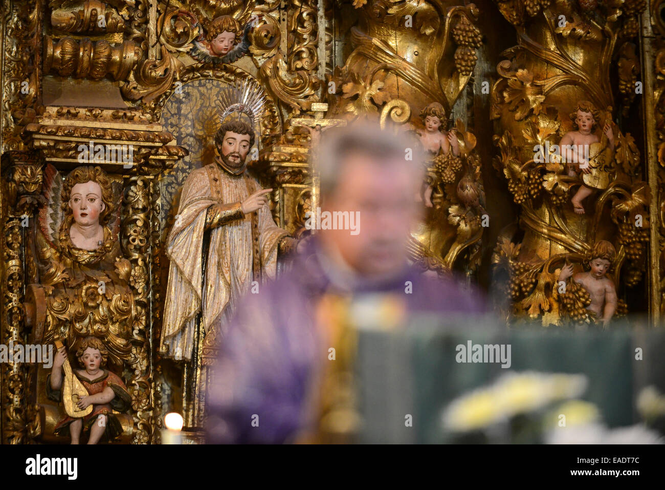 Statues of saints and angels on an ornate altar behind a catholic priest celebrating mass Stock Photo