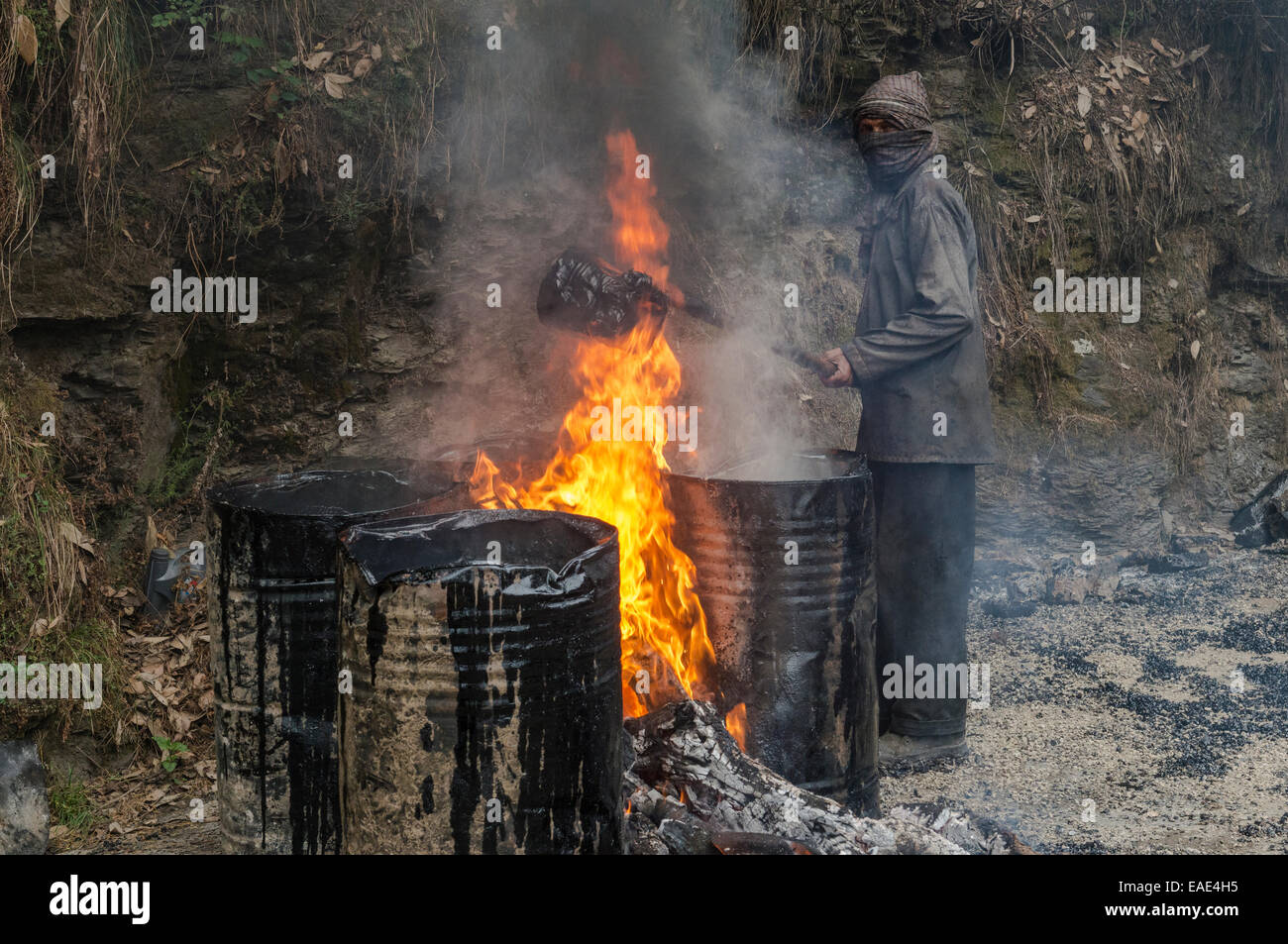A worker heating tar in barrels with an open fire at a road construction site, Shimla, Himachal Pradesh, India Stock Photo