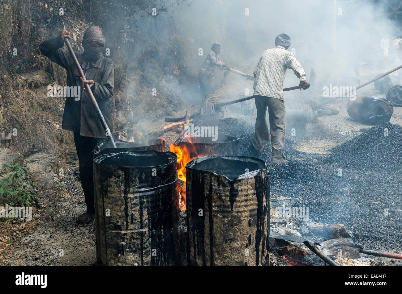 A worker heating tar in barrels with an open fire at a road construction site, Shimla, Himachal Pradesh, India Stock Photo