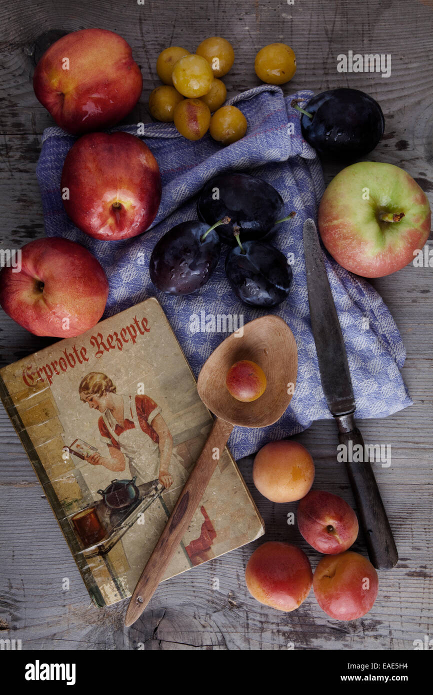 Kitchen scene, old cookbook, apples, prunes, plums, apricots and nectarines on a wooden surface Stock Photo