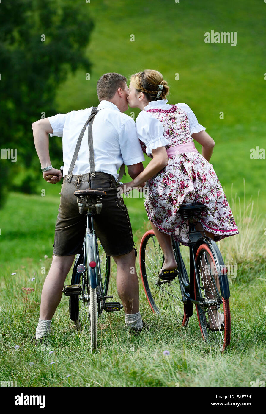 Man wearing leather pants and a woman wearing a dirndl kissing on