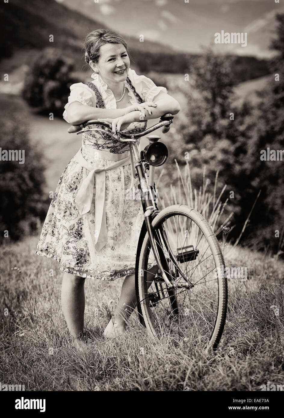 Woman wearing a dirndl with an old bicycle, Igls, Innsbruck, Tyrol, Austria Stock Photo