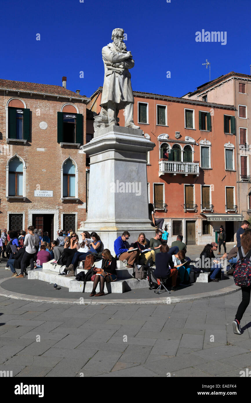 Students sat below the statue of Nicolo Tommaseo in Campo Santo Stefano, Venice, Italy. Stock Photo