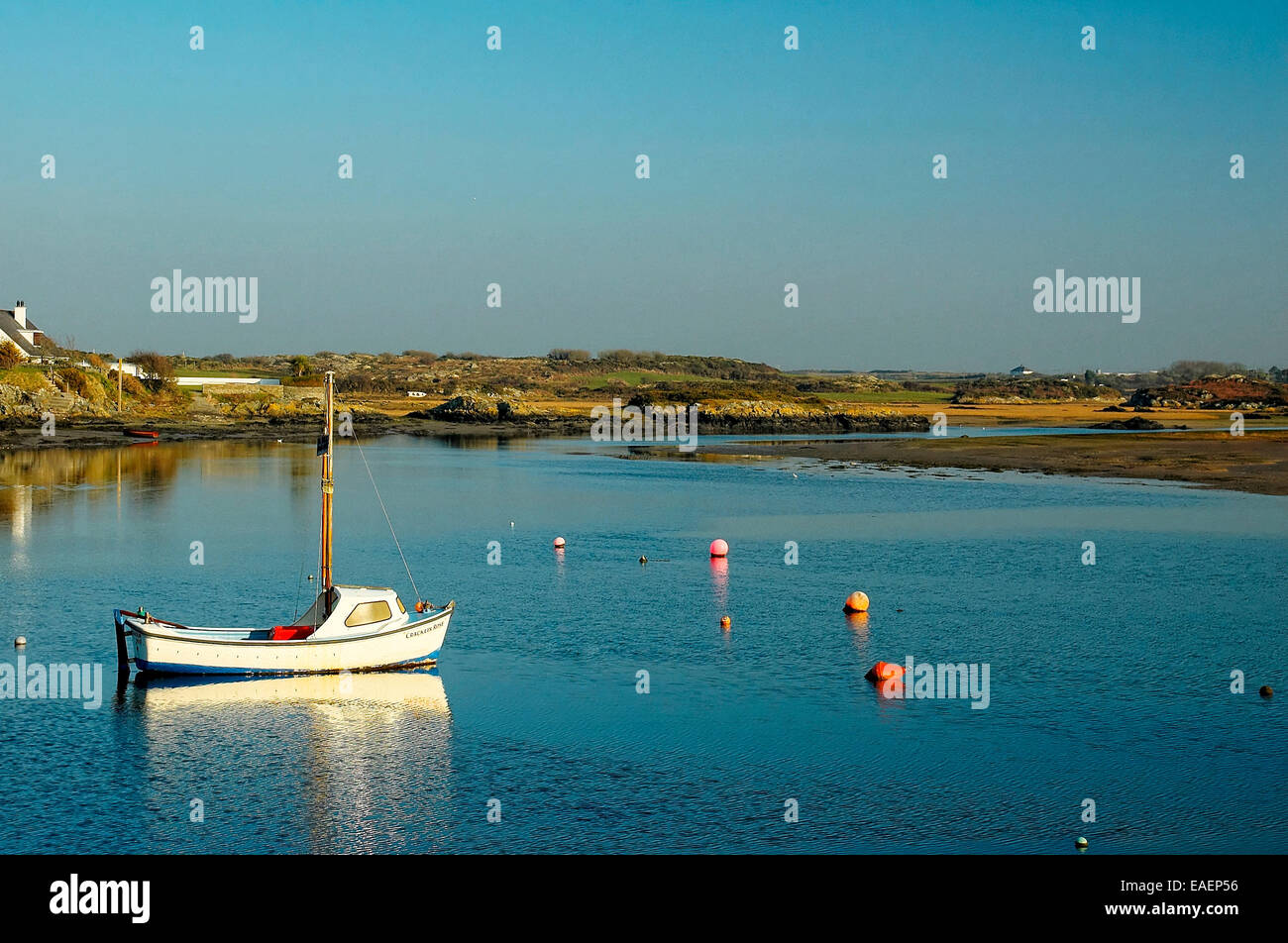 A single boat floats calmly in the estuary of the Inland Sea at Four Mile Bridge, Anglesey, Wales Stock Photo