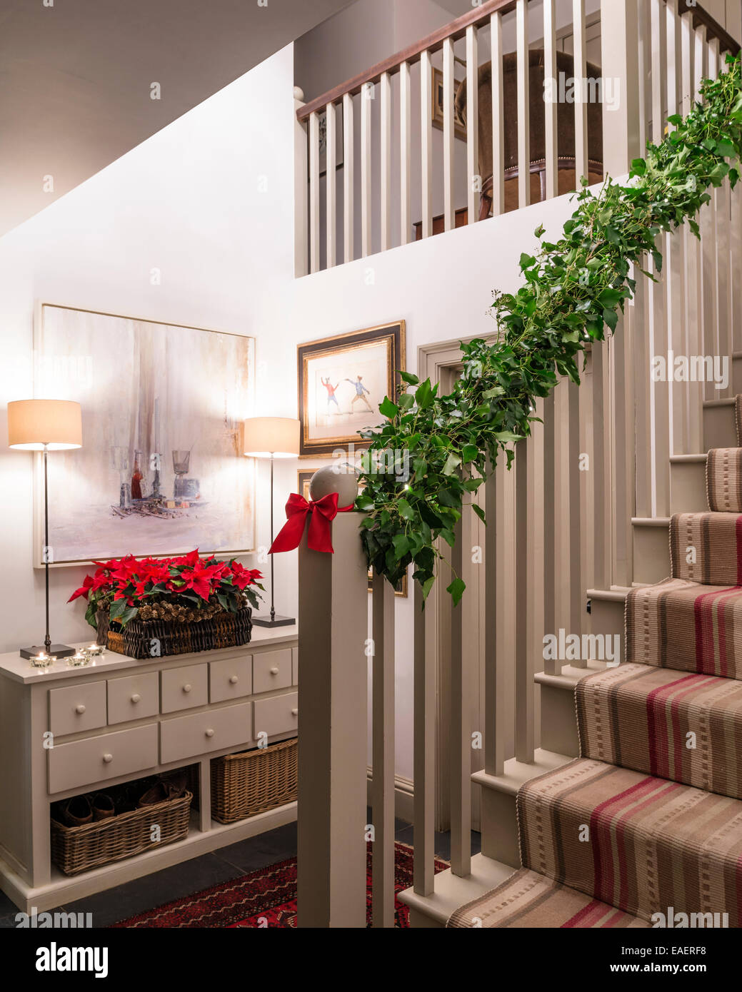 Ivy wrapped around stair banister and tray of poinsettas adds a festive seasonal touch to a hallway Stock Photo