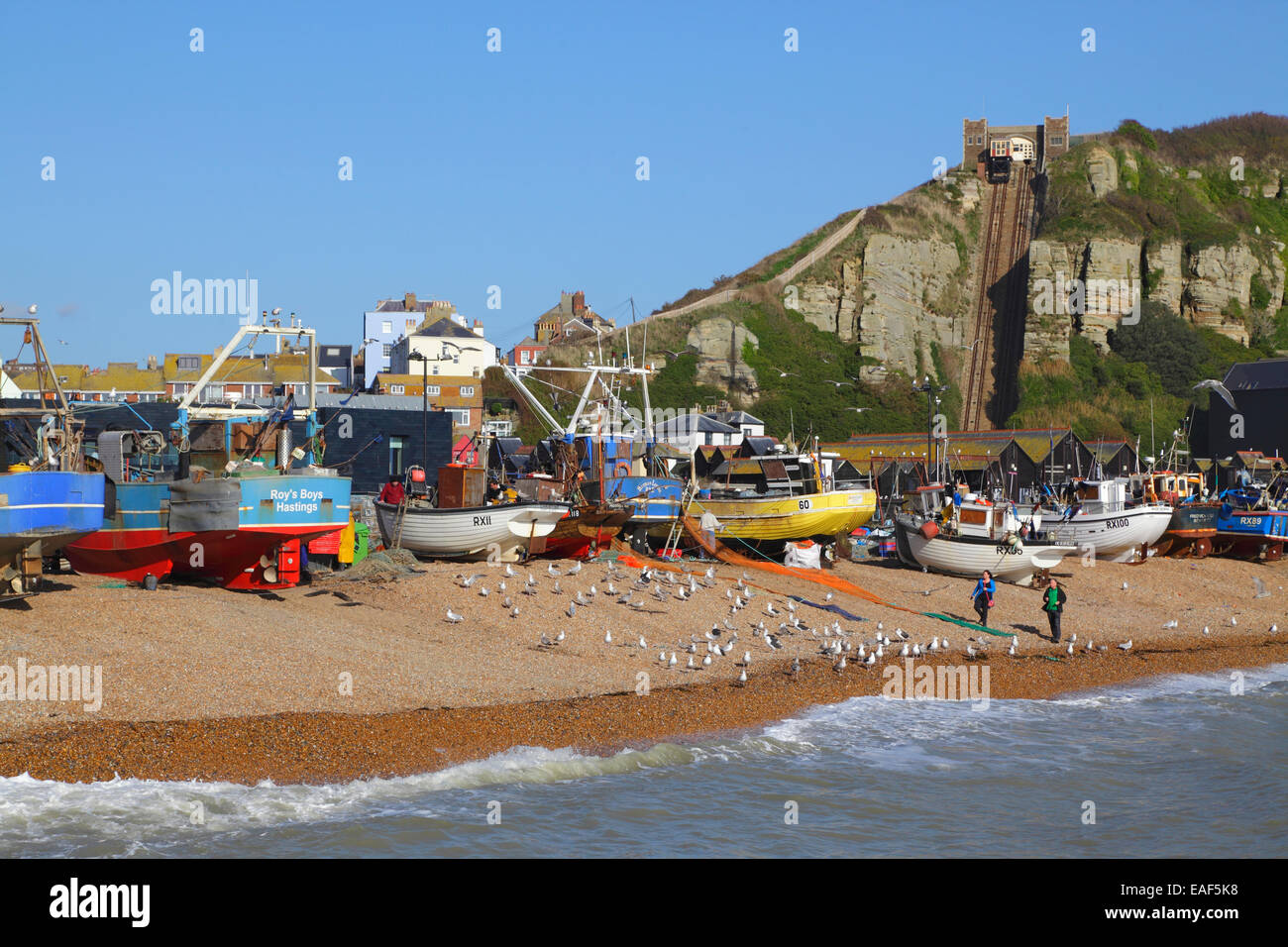 Couple walking on Hastings Old Town Stade beach, in front of the fishing boats and the Hastings Contemporary Art Gallery, East Sussex, UK. Stock Photo