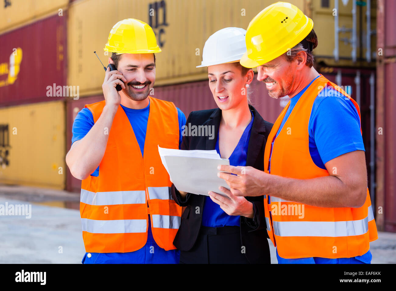 Worker and manager of shipment company discussing freight or shipment documents, one man is using phone or walkie-talkie Stock Photo