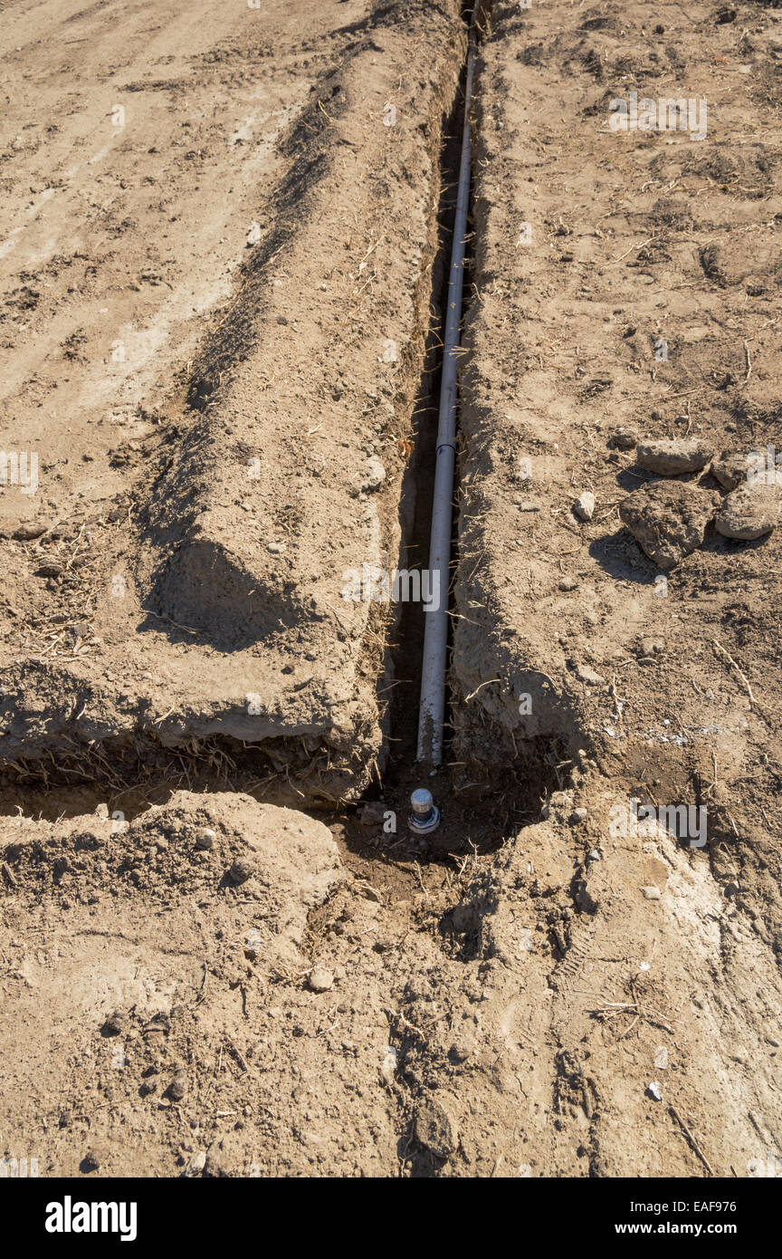 irrigation system installation with pvc pipes in trenches in a soil field Stock Photo