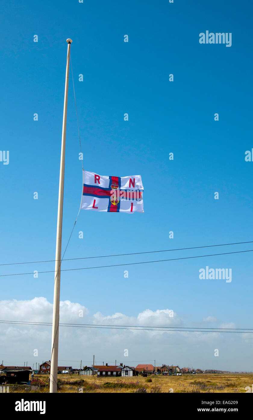 RNLI flag flying at half-mast in front of the lifeboat station on Dungeness Beach, Kent Stock Photo