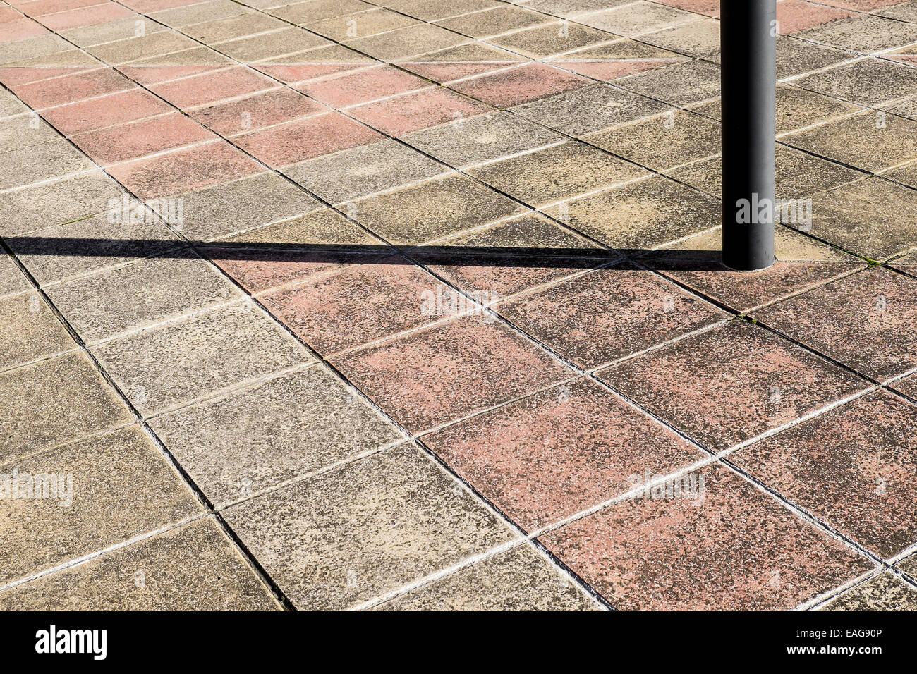 A post casting a shadow across paving slabs. Stock Photo